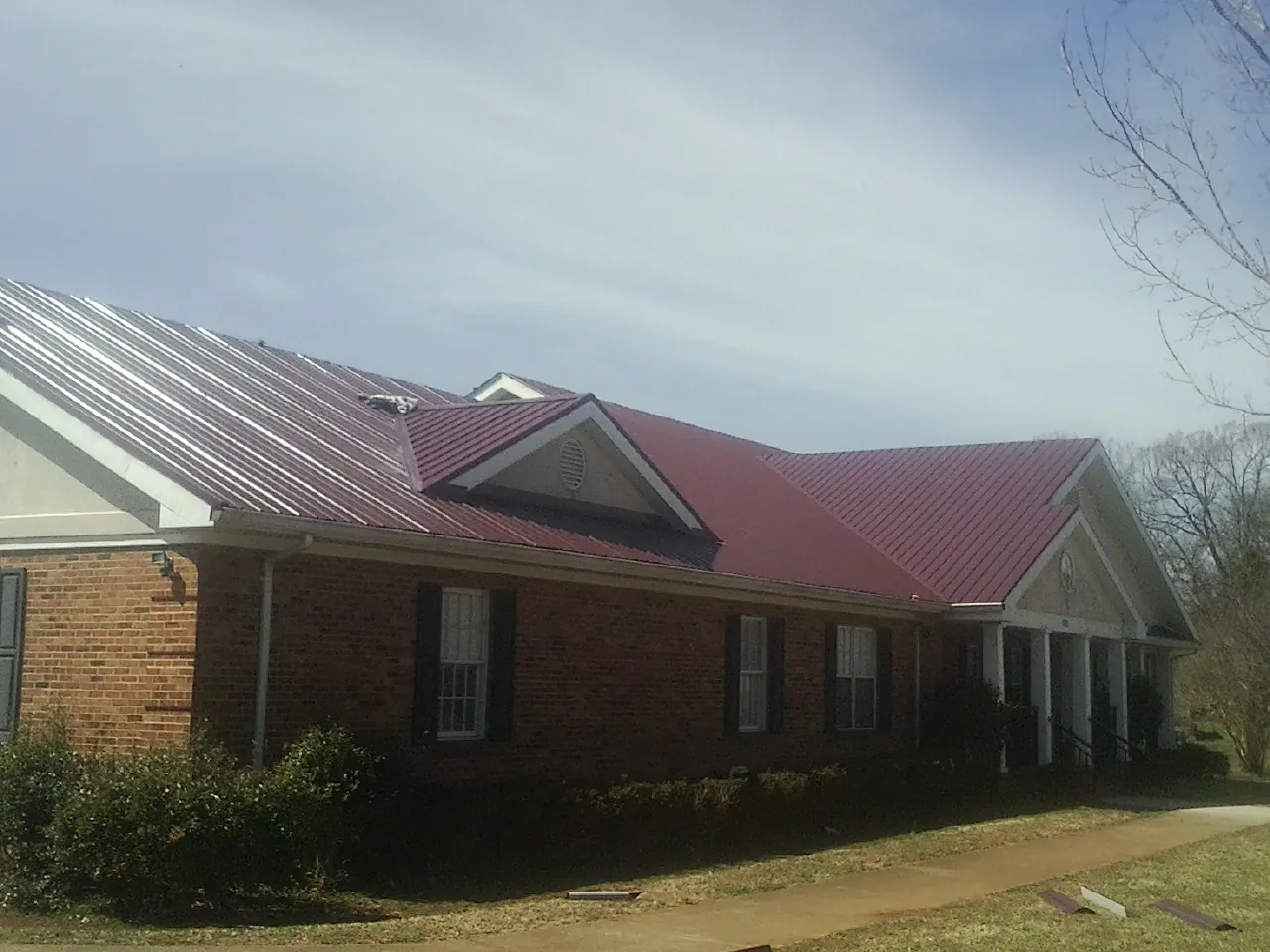 Red metal roof with gabled entries on a long brick building, from a Hail Damage Roof Repair job in Plymouth Meeting