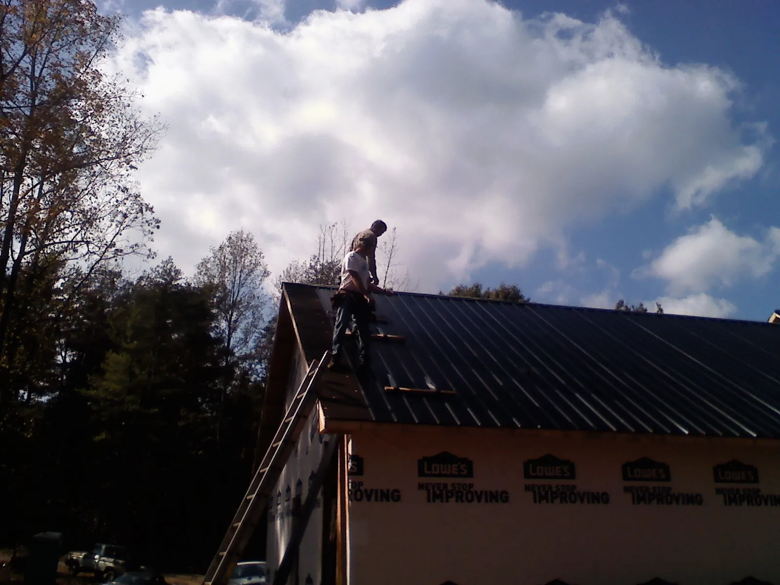 Roofer fastening dark metal panels high against a cloudy sky, from a Roof Inspection job in Plymouth Meeting
