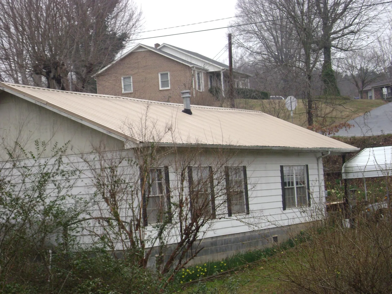 Tan metal roof on a white sided house set into a hillside — Commercial Roofing by Roofing Brothers in Plymouth Meeting